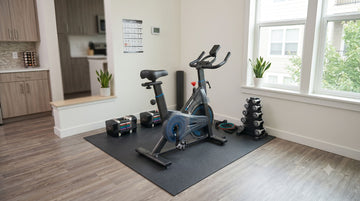 Ein komplettes, preiswertes Einsteiger-Homegym mit einem Wenoker JC302 Heimtrainer, verstellbaren Gewichten und einer robusten PVC-Matte in der Ecke einer kleinen Wohnung